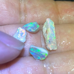 Könnte beinhalten: Vier kleine, schillernde Opal-Steine in verschiedenen Formen und Größen. Die Steine sind eine Mischung aus Weiß, Blau, Grün und Gelb.