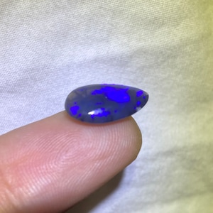Könnte beinhalten: Ein dunkelgrauer Opal-Cabochon mit blauen und weißen Farbschimmern.