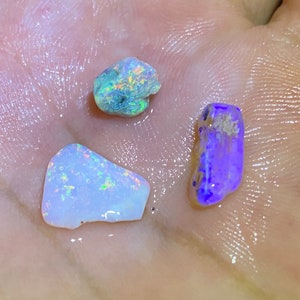 Könnte beinhalten: Drei kleine, schillernde Opal-Steine. Die Steine sind in verschiedenen Blautönen, Grüntönen und Weißtönen.