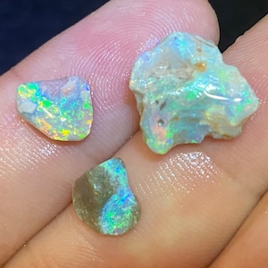 Può includere: Tre pietre di opale grezze e naturali in varie tonalità di verde, blu e bianco. Le pietre sono iridescenti e hanno una finitura naturale non lucidata.