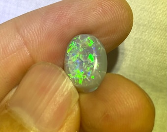 May include: A light gray oval opal gemstone with green and blue iridescent flashes.