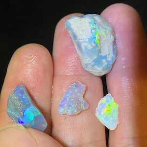 Könnte beinhalten: Vier Stücke rohen Opals, ein großes und drei kleinere, mit schillernden Farben in Blau, Grün und Gelb.