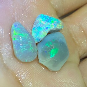 Könnte beinhalten: Drei schillernde Opal-Steine in verschiedenen Formen und Größen. Die Steine sind hellblau-grau mit grün-blauen Schimmern.