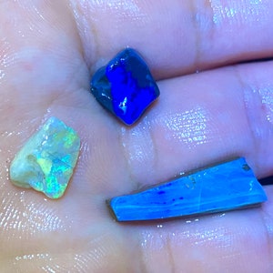 May include: Three pieces of opal, one is a dark blue, one is a light blue, and one is a white opal with a yellow and green iridescent sheen.