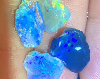 May include: Four pieces of opal, one is a dark blue, one is a light blue, one is a light green, and one is a light blue with a rainbow sheen.