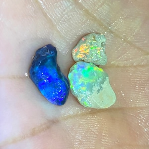 Könnte beinhalten: Drei rohe Opal-Edelsteine, einer blau, einer grün und einer weiß mit Regenbogen-Irisieren.