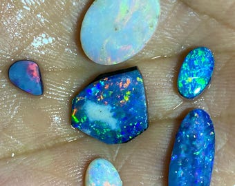 May include: A collection of opals in various shapes and sizes, showcasing vibrant blue, green, and iridescent colors. The gemstones are displayed on a hand, highlighting their natural beauty and unique patterns. The opals range from oval to irregular shapes.