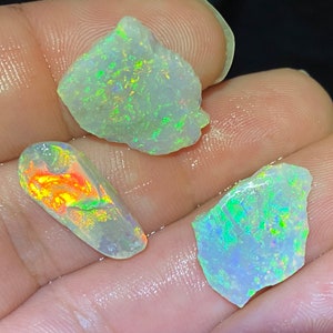 Könnte beinhalten: Drei Stücke roher Opal, eines ist hellgrün, eines hellblau und eines hellorange. Die Opale sind irisierend und haben eine Vielzahl von Farben.