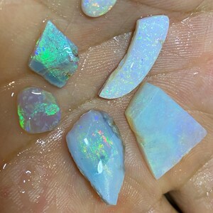 May include: A collection of opals in various shapes and sizes. The opals display a range of colors, including blue, green, and flashes of iridescent hues. The gemstones are raw and uncut, showcasing their natural beauty.