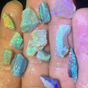 Könnte beinhalten: Eine Sammlung kleiner, rauer, irisierender Opal-Edelsteine in verschiedenen Blautönen, Grüntönen und Violett.