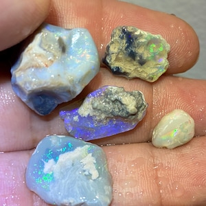 May include: A collection of raw opals in various shapes and sizes, showcasing a spectrum of colors. The opals display iridescent flashes of blue, green, and yellow against a milky white and gray background. Some opals have rough, textured exteriors.