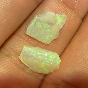 May include: Two rough, natural, white opal gemstones with green and blue iridescence.
