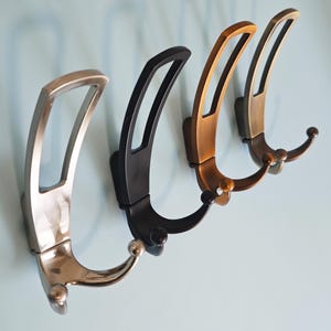 May include: Four metal coat hooks in a row, each with a different finish: brushed nickel, black, bronze, and antique brass. The hooks have a curved design with a decorative ball at the end of the hook.