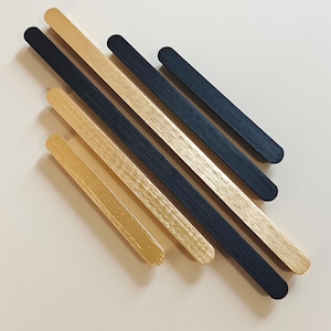 May include: An arrangement of six wooden sticks in gold and navy blue, arranged at an angle. The sticks are flat and rectangular with rounded ends. The wood grain is visible, adding texture to the design. The overall aesthetic is modern and minimalist.
