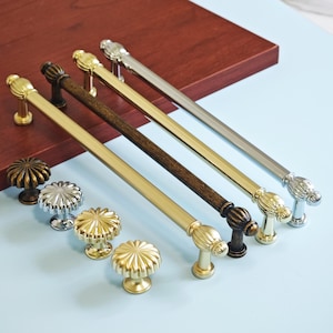 May include: A collection of cabinet hardware, including various styles of drawer pulls and knobs. The drawer pulls are available in gold, bronze, and silver finishes. The knobs have a fluted design.