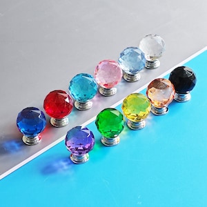May include: A selection of colourful crystal ball cabinet knobs. The knobs are in various colours, including blue, red, green, and purple, with a faceted design. Each knob is mounted on a silver base.