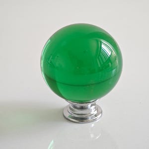 May include: A bright green glass sphere cabinet knob with a polished chrome base. The spherical knob reflects light, creating a glossy appearance. This decorative hardware adds a pop of colour and modern style to furniture.