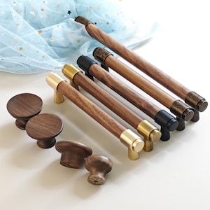 Pode incluir: Uma coleção de ferragens de madeira para armários, incluindo puxadores redondos e puxadores de barra. Os puxadores de barra têm extremidades metálicas em latão, preto e bronze. Os puxadores são de madeira escura. Medidas em cm.