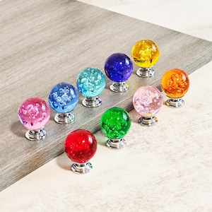 May include: A collection of ten colorful glass cabinet knobs. Each knob features a clear, bubble-filled sphere in shades of red, pink, blue, green, yellow, and orange, mounted on a silver-toned base. These decorative knobs are ideal for adding a pop of color.