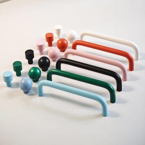 Peut inclure: Une collection de quincaillerie d'armoires colorées, comprenant des boutons et des poignées. Les boutons sont de différentes formes et couleurs, comme le blanc, le rouge, le rose, le noir, le vert et le bleu. Les poignées sont incurvées et sont disponibles en blanc, rouge, rose, noir, vert et bleu clair.