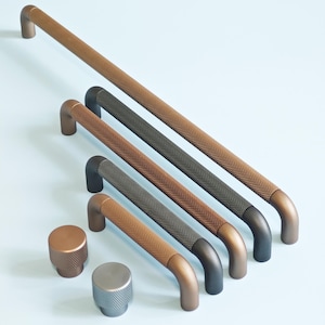 May include: A collection of textured metal cabinet pulls and knobs in various colors, including bronze, dark gray, and silver. The pulls have a curved handle design, and the knobs are round with a textured surface.