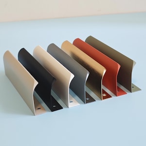 Op de afbeelding: Een verzameling van zeven metalen plankdragers in verschillende kleuren, waaronder beige, zwart, crème, grijs, brons, rood-oranje en olijfgroen. Elke beugel heeft een haakse vormgeving met een platte basis en een gebogen voorrand.