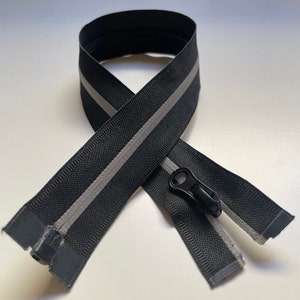 May include: Black zipper tape with a reflective silver stripe down the centre. The zipper tape is folded in half and the zipper pull is visible.