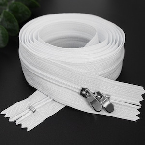 May include: White zipper tape with a silver zipper pull. The zipper is coiled up and ready to be sewn into a garment.