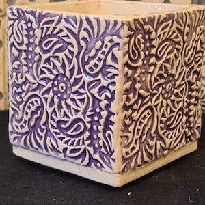 Może przedstawiać: Kwadratowa doniczka ceramiczna z białym tłem i fioletowym wzorem paisley.