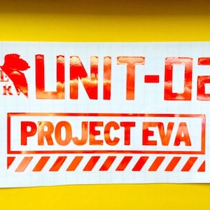 May include: Red and white sticker with the text "UNIT-02 PROJECT EVA" in a bold, blocky font. The sticker has a red and white striped border.