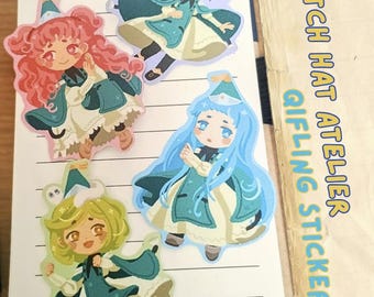 Könnte beinhalten: Vier gestanzte Aufkleber mit Chibi-Figuren in türkisfarbenen und weißen Hexenoutfits mit spitzen Hüten, angeordnet auf einem linierten Notizblock. Der Text WITCH HAT ATELIER QIFLING STICKERS ist in Blau auf der rechten Seite des Blocks gedruckt.