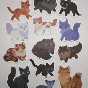 May include: A selection of cat stickers in diverse colours and patterns. The stickers depict various cat breeds and poses, including tabby, calico, and solid-coloured cats. The stickers are set against a white background.