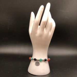 May include: A bracelet featuring red, green and black beads with a silver charm depicting a lotus flower.