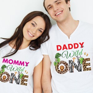 May include: White t-shirts with safari-themed graphics. One shirt reads "MOMMY of the Wild ONE" in pink and green, featuring a lion, zebra, and leopard print. The other shirt says "DADDY of the Wild ONE" in red and green, with similar animal prints.