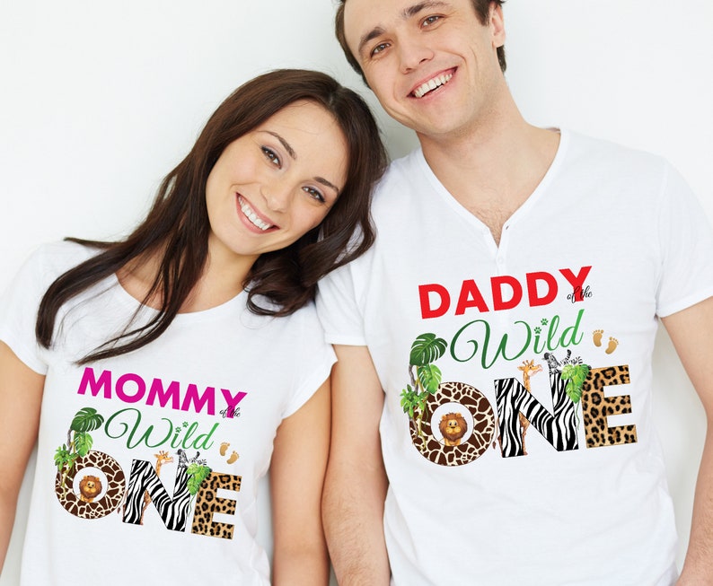 May include: White t-shirts with safari-themed graphics. One shirt reads "MOMMY of the Wild ONE" in pink and green, featuring a lion, zebra, and leopard print. The other shirt says "DADDY of the Wild ONE" in red and green, with similar animal prints.