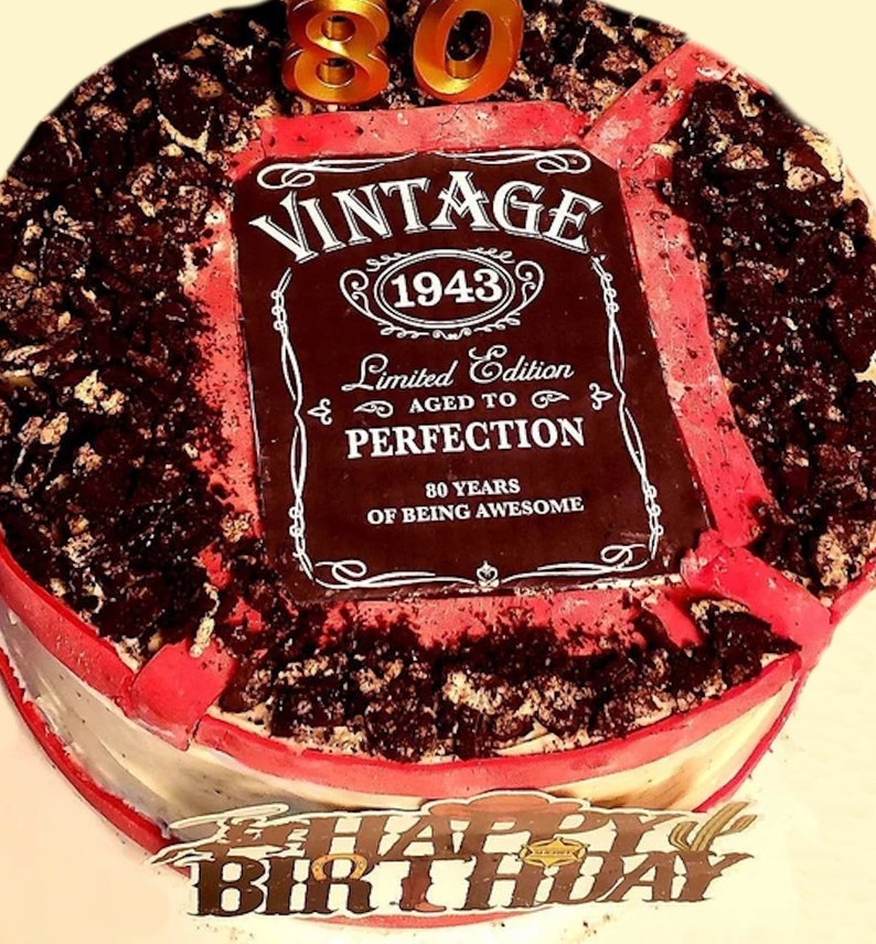 May include: A red and white cake decorated with a black and white label that says "Vintage 1943 Limited Edition Aged to Perfection 80 Years of Being Awesome". The cake is also decorated with chocolate sprinkles and a gold number 80 candle.