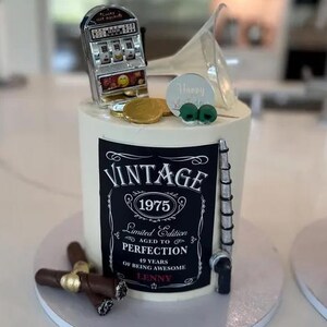 May include: A black and white cake with a vintage label that says "Vintage 1975 Limited Edition Aged to Perfection 49 Years of Being Awesome Lenny". The cake is decorated with a slot machine, a martini glass, and cigars.