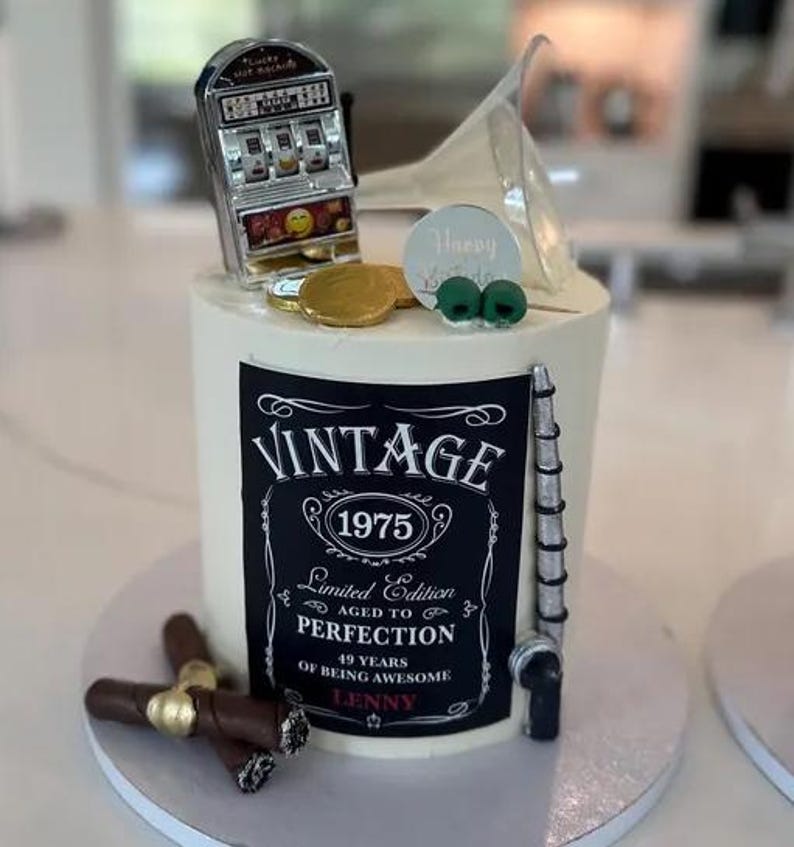 May include: A black and white cake with a vintage label that says "Vintage 1975 Limited Edition Aged to Perfection 49 Years of Being Awesome Lenny". The cake is decorated with a slot machine, a martini glass, and cigars.