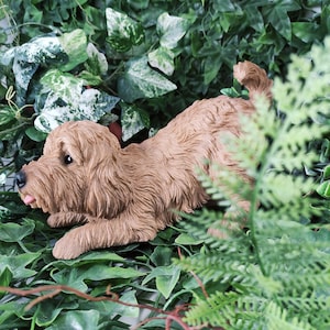 May include: A brown, furry dog figurine lying in a bed of green leaves. The dog has a long snout and floppy ears.