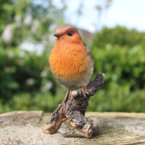 May include: A small, realistic figurine of a robin perched on a branch. The robin is orange and brown with a white breast. The branch is brown and textured.