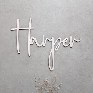 A personalised wooden name sign in a handwritten calligraphy design, in this example for Harper. The name is cut from birch plywood in our Ash font.  The wooden name is presented on a neutral background with dried flower accents.