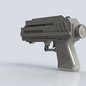 K&ouml;nnte beinhalten: Eine hellgraue, futuristisch aussehende Pistole mit einem rechteckigen Oberteil und einem kreisf&ouml;rmigen Element an der Seite. Der Griff hat eine abgerundete Form mit einem kreisf&ouml;rmigen Design. Das Gesamtdesign deutet auf ein Science-Fiction- oder Cosplay-Requisit hin.