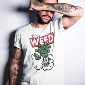 Peut inclure: T-shirt blanc avec l'inscription "Enjoy WEED" en rouge et blanc. Une main de dessin animé tient un pot de feuilles de cannabis vertes avec l'étiquette "KUSH". Fond blanc.