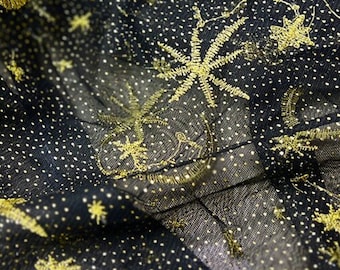 May include: A sheer black fabric featuring a dense pattern of tiny white dots and embroidered gold thread motifs. The embroidery depicts various celestial shapes, including crescent moons and multi-pointed stars, scattered across the surface.