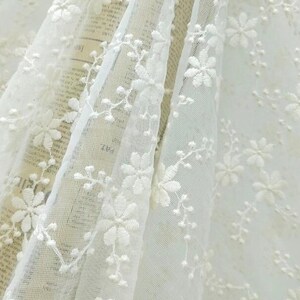 May include: White embroidered tulle fabric with a delicate floral pattern. The fabric is sheer and lightweight, making it ideal for crafting and sewing projects.