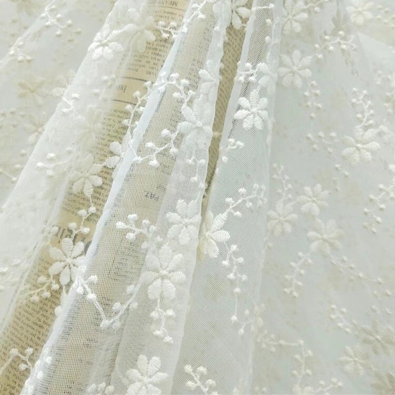 May include: White embroidered tulle fabric with a delicate floral pattern. The fabric is sheer and lightweight, making it ideal for crafting and sewing projects.
