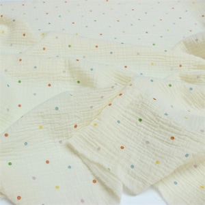 May include: Off-white fabric with a crinkled texture, adorned with small, multi-coloured polka dots. The dots are in shades of red, green, blue, and yellow. The fabric is folded, displaying its soft, flowing quality. Suitable for various craft projects.