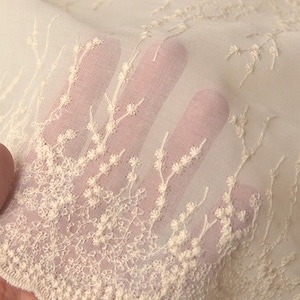 Peut inclure: Tissu blanc ivoire transparent avec de d&eacute;licats motifs floraux brod&eacute;s. Le tissu est doux, a&eacute;r&eacute; et parfait pour cr&eacute;er des v&ecirc;tements l&eacute;gers.