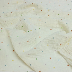 May include: Off-white fabric with a crinkled texture, adorned with small, multi-coloured polka dots. The dots are in shades of red, orange, yellow, green, blue, and purple. The fabric is folded, revealing its layered construction and soft feel.