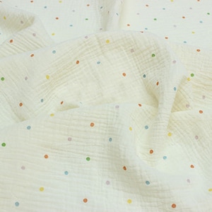 May include: Cream-colored muslin fabric with a crinkled texture, scattered with small, colorful polka dots in shades of orange, yellow, green, and blue. The fabric is soft and appears lightweight, suitable for various sewing projects.